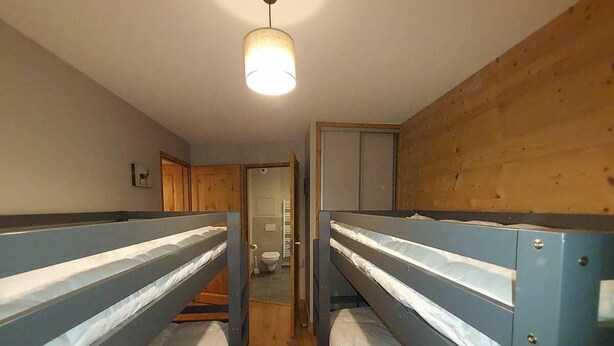 Une chambre de dortoir avec des lits superposés, des murs en bois, un luminaire au plafond et une porte donnant sur une salle de bain.