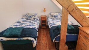 Une petite pièce étroite, avec deux lits, une table de chevet en bois et un plafond en pente.