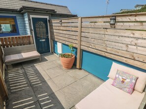 Une terrasse avec une clôture en bois, un banc, un pot de fleurs et un fauteuil de jardin.
