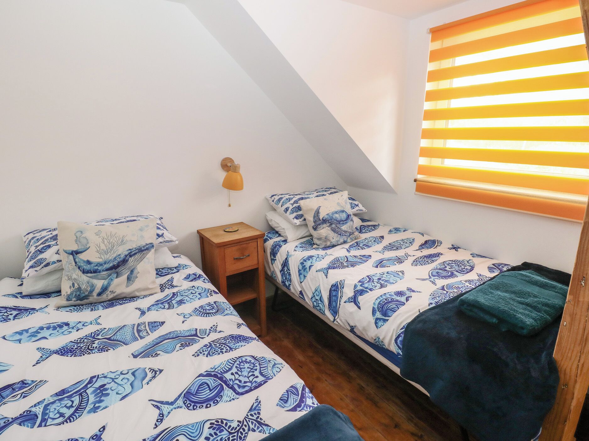 Un dormitorio con dos camas, una mesita de noche, una lámpara y una ventana con persianas.