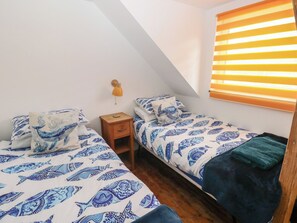 Une chambre avec deux lits, une table de chevet, une lampe et une fenêtre avec des stores.