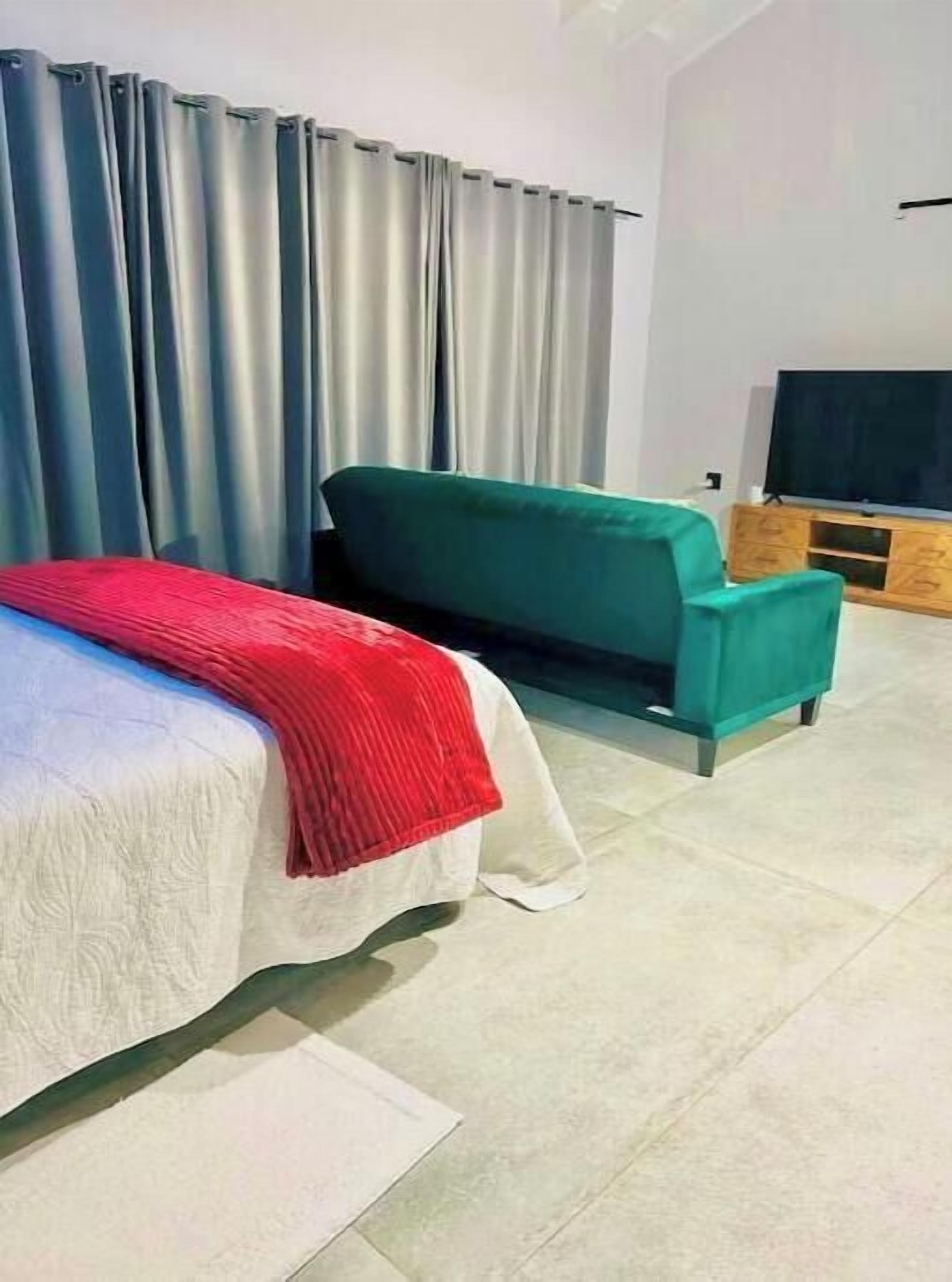 Ein Zimmer mit einem Bett, einem grünen Sofa, einem Fernseher auf einem Holzboden und einem Fenster mit Vorhängen.