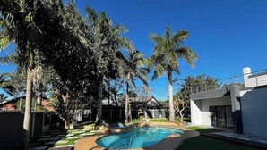 Una casa moderna con piscina rodeada de césped artificial y palmeras.