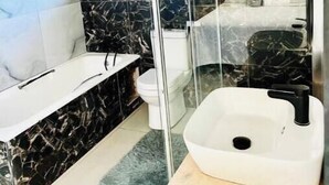 Een moderne badkamer met een douchecabine van glas, een witte wastafel en een marmeren aanrecht.