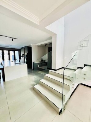 A modern interior with a staircase leading to a second floor, a kitchen area, and a dining space. - Private apartment, La Casa Villa luxury at the Bay (Richards Bay)