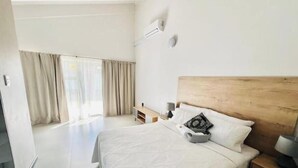Een slaapkamer met een groot bed, een houten hoofdbord, een nachtkastje met een lamp en een raam met gordijnen.