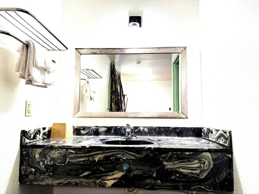 Un bany amb un lavabo de marbre, un mirall i una barra de tovalloles.