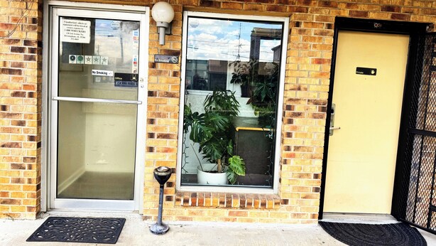 A brick building with a glass door, a window with a potted plant, and a yellow door. - Southern Comfort Motel (Birmingham)