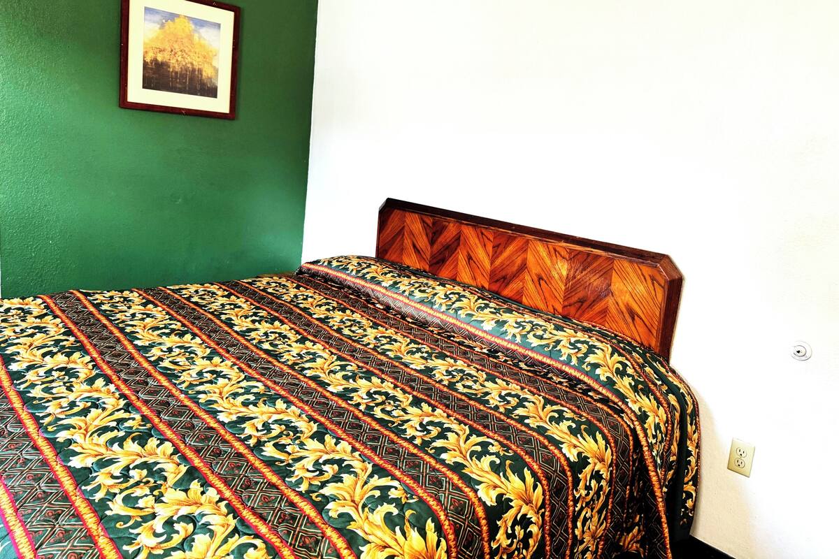 A bed with a patterned bedspread, a framed picture on the wall, and a white wall.