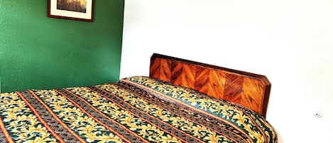 A bed with a patterned bedspread, a framed picture on the wall, and a white wall.