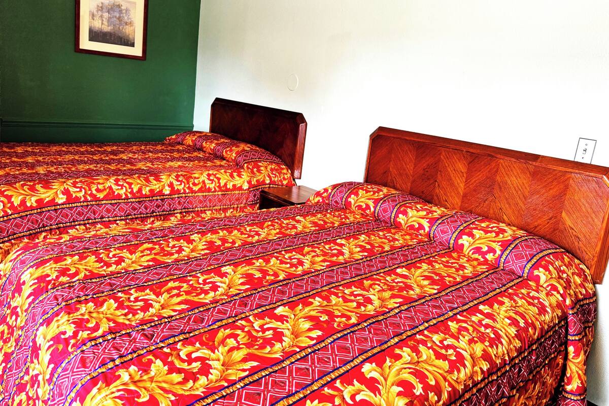 A room with two beds, each with a patterned bedspread, a framed picture on the wall, and a wooden headboard.