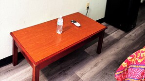 A room with a flat-screen TV mounted on the wall, a wooden table with a bottle and a remote control, and a black speaker. - Southern Comfort Motel (Birmingham)