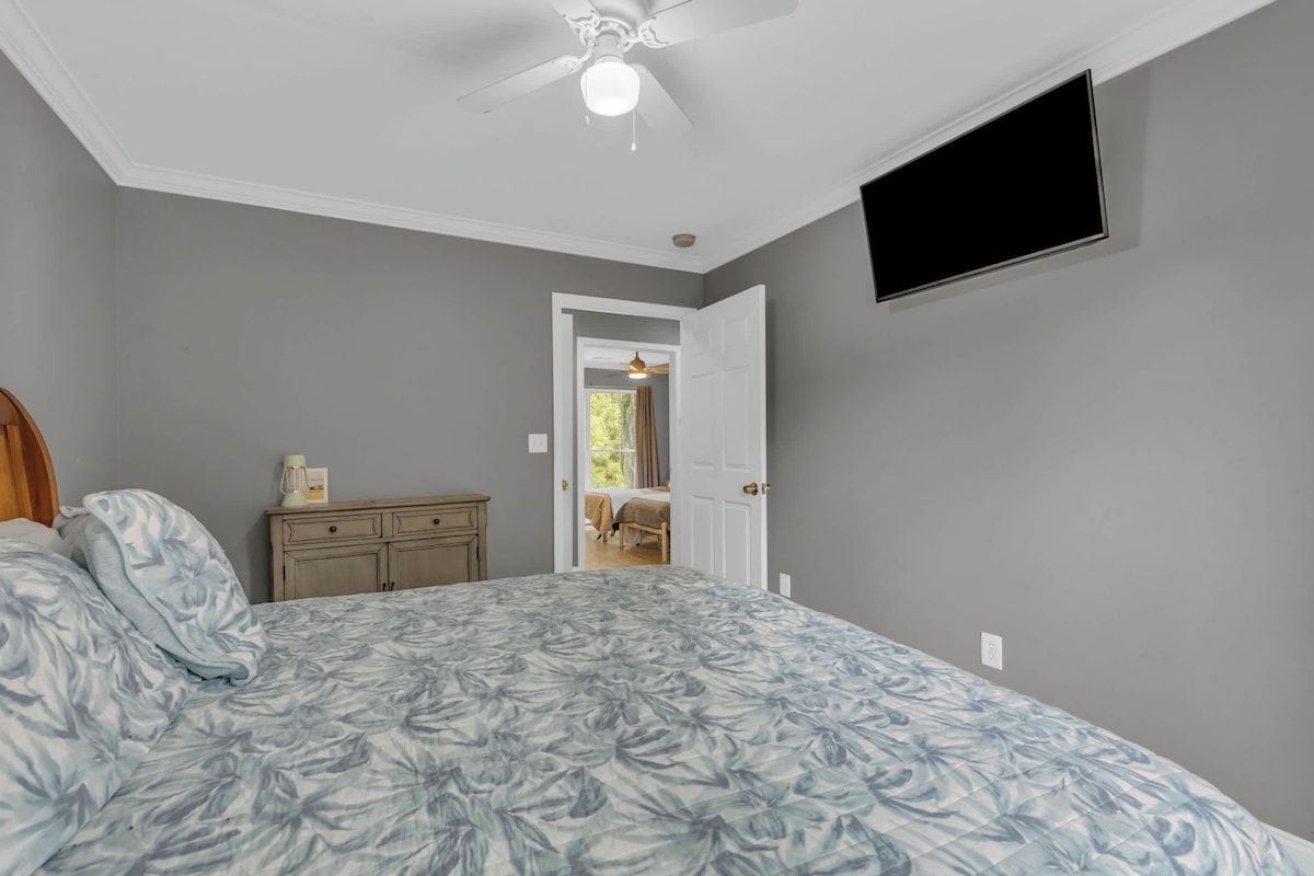 Une chambre à coucher comprenant un lit, une commode, un ventilateur de plafond et un téléviseur fixé au mur.