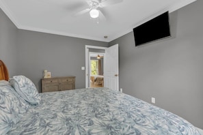 A bedroom with a bed, a dresser, a ceiling fan, and a TV mounted on the wall.