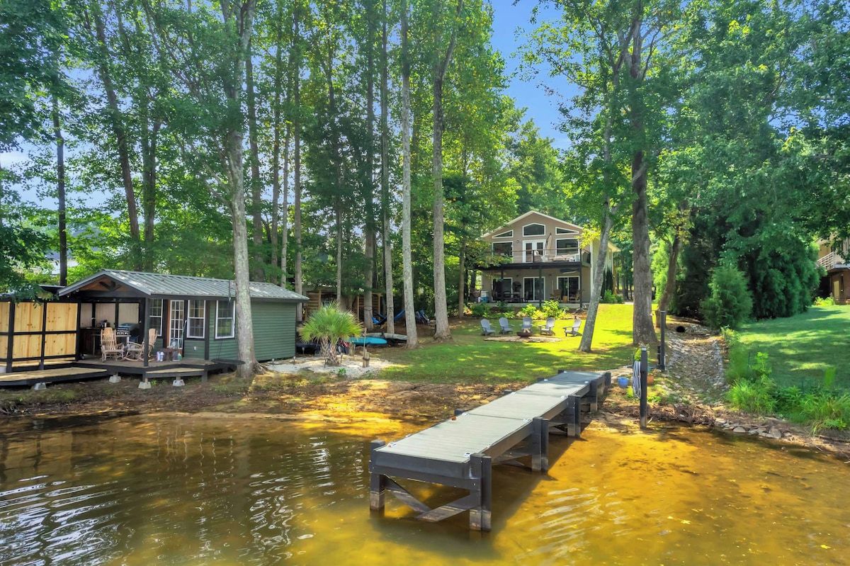 A lakeside property with a dock, a small cabin, and a larger house surrounded by trees.