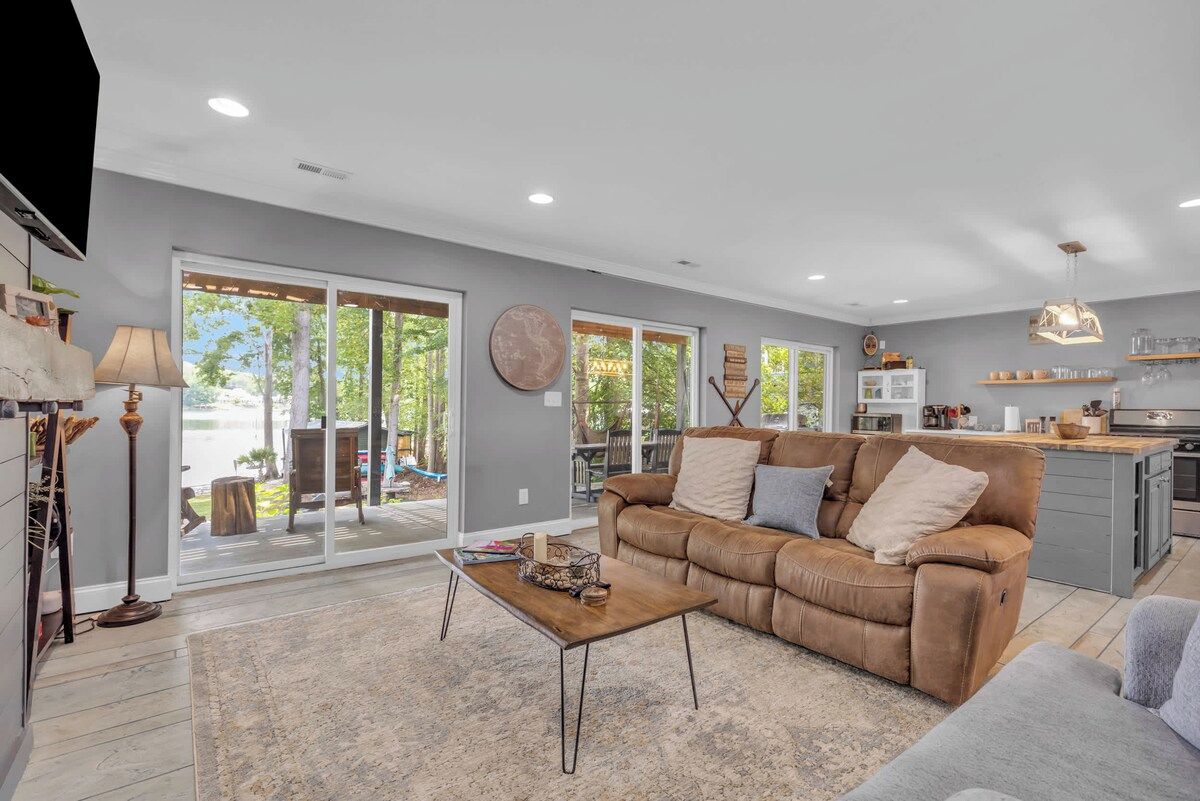 A spacious living room with a brown leather sofa, a coffee table, and a large window offering a view of the outdoors.