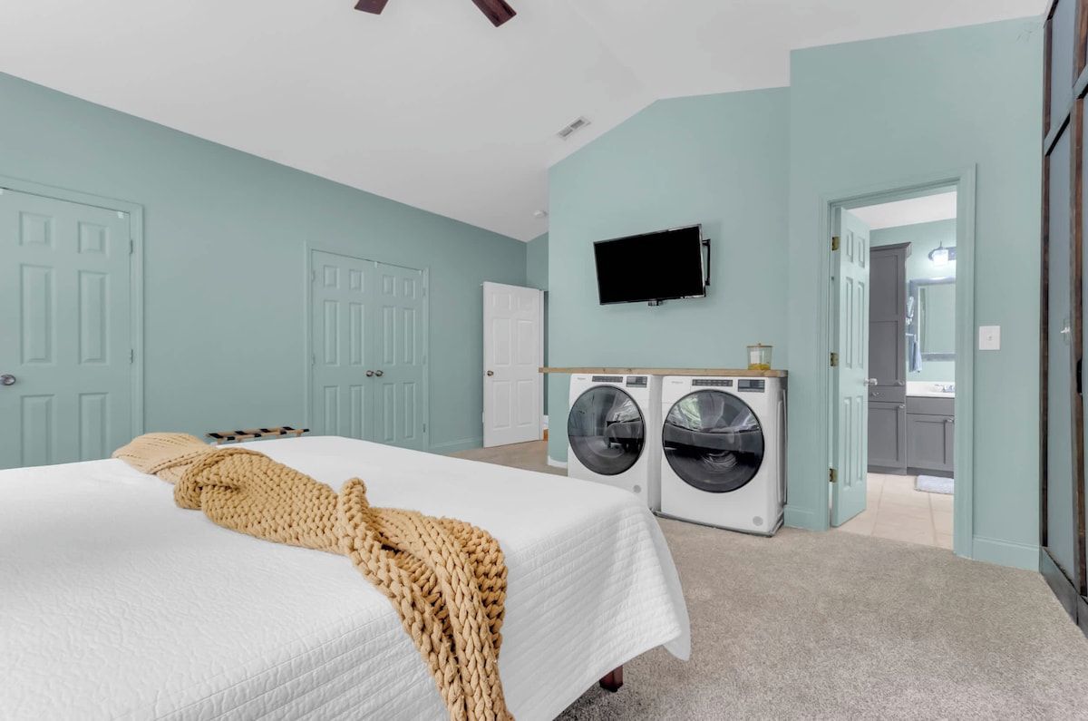 A bedroom with a bed, a washing machine, and a television.