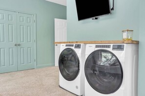 A laundry area with two front-loading washing machines, a television mounted on the wall, and a white door.