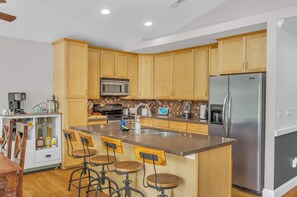 Cocina con armarios de madera, refrigerador de acero inoxidable, microondas y cafetera. Hay tres taburetes en la isla.