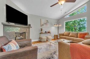 Una sala de estar con chimenea, televisor, sofá y un amplio ventanal.