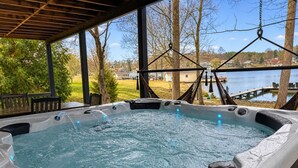 A hot tub with a wooden deck and a view of a lake and houses.