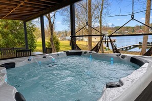 Jacuzzi con muelle de madera y vista a un lago y casas.
