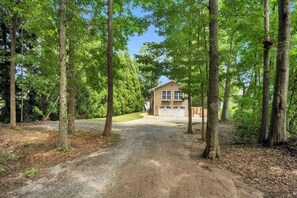 A house with a garage, surrounded by tall trees and a gravel driveway.