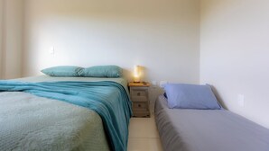 Un dormitorio pequeño y bien iluminado con dos camas, una mesita de noche y una lámpara de pared.