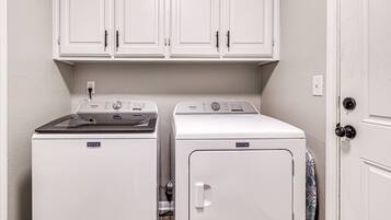 Une buanderie équipée d’un lave-linge et d’un sèche-linge Maytag, d’une cuisinière et de placards blancs situés en hauteur.