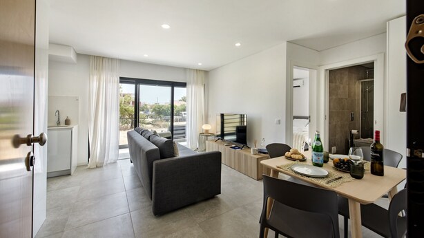 A modern living room with a sofa, dining table, and TV. There is a balcony with a view of the city.