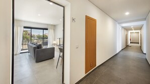 A modern hotel corridor with a wooden door, a sofa, and a view through a glass door.
