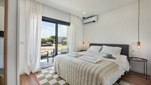 A modern bedroom with a large bed, a view through a glass door, and a ceiling fan.