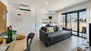 A modern living room with a grey sofa, dining table, and a kitchen in the background.