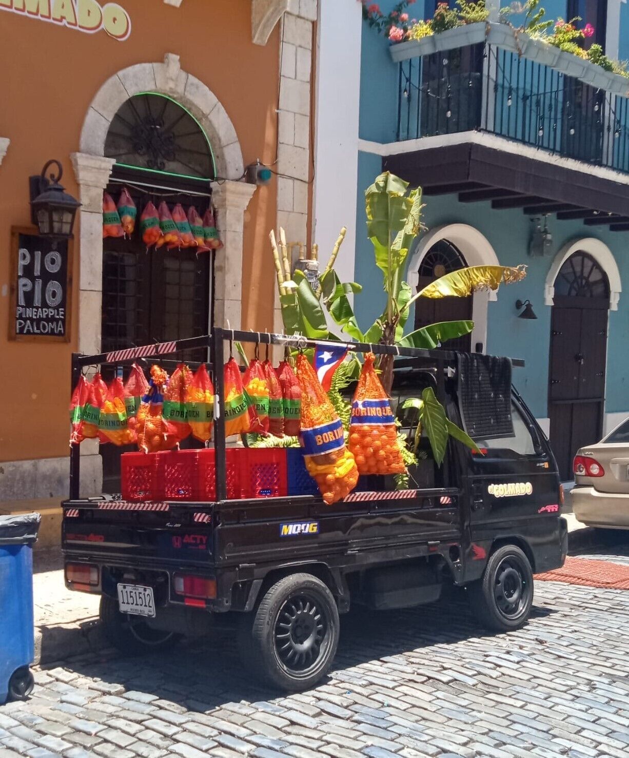 Una camioneta negra cargada de bolsas de naranjas estacionada en una calle adoquinada.