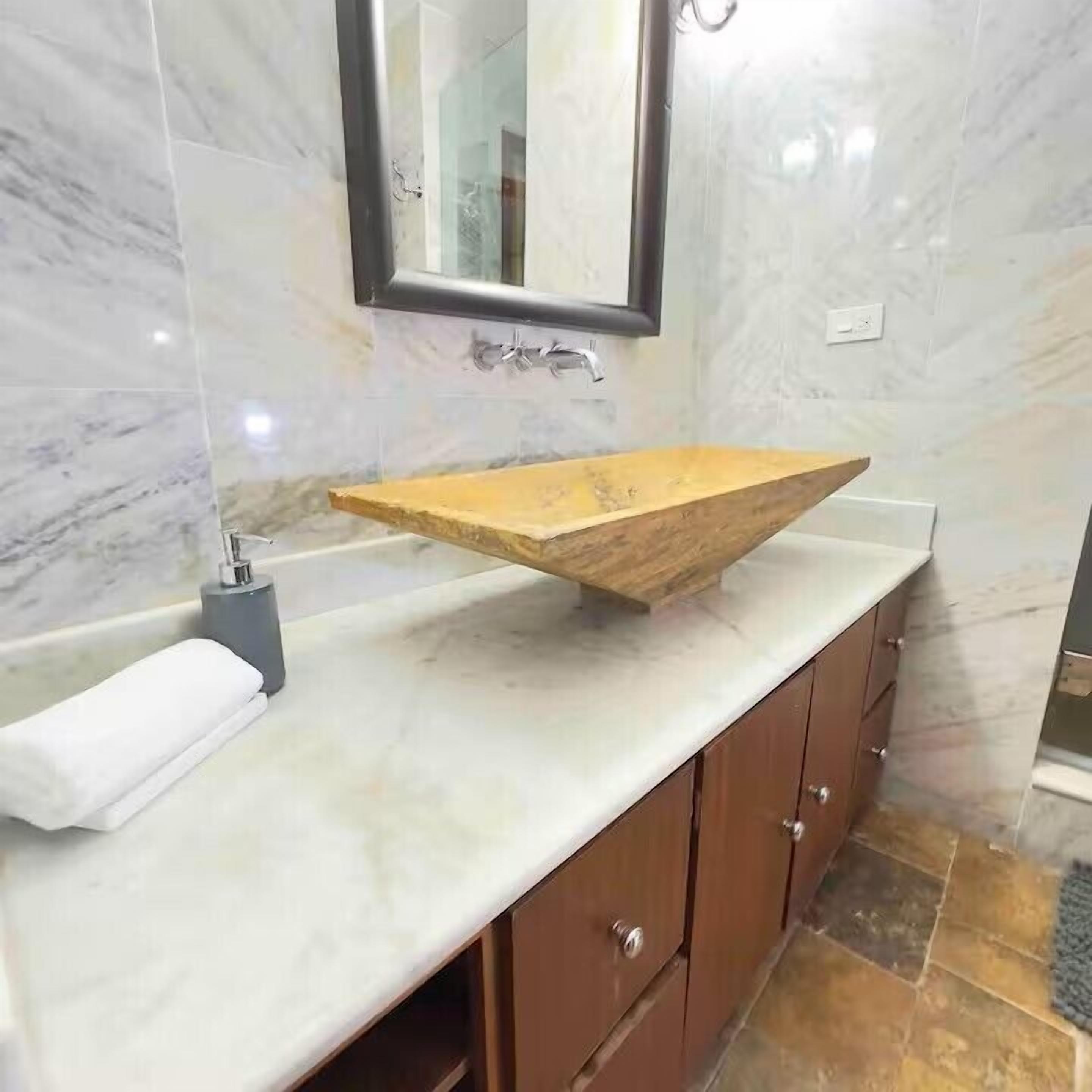 A bathroom with a wooden vanity, marble tiles, and a mirror.