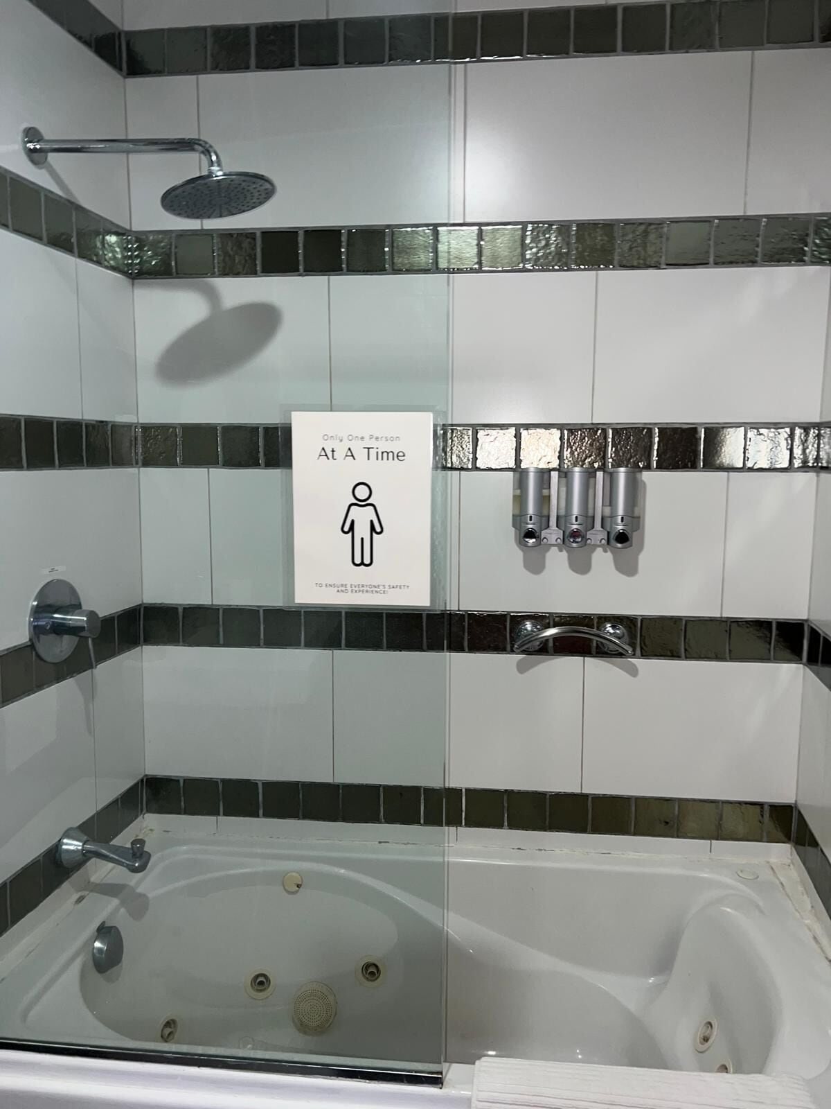 Et badeværelse med brusebad, et skilt der står 'Adgang for én person ad gangen', og et badekar.