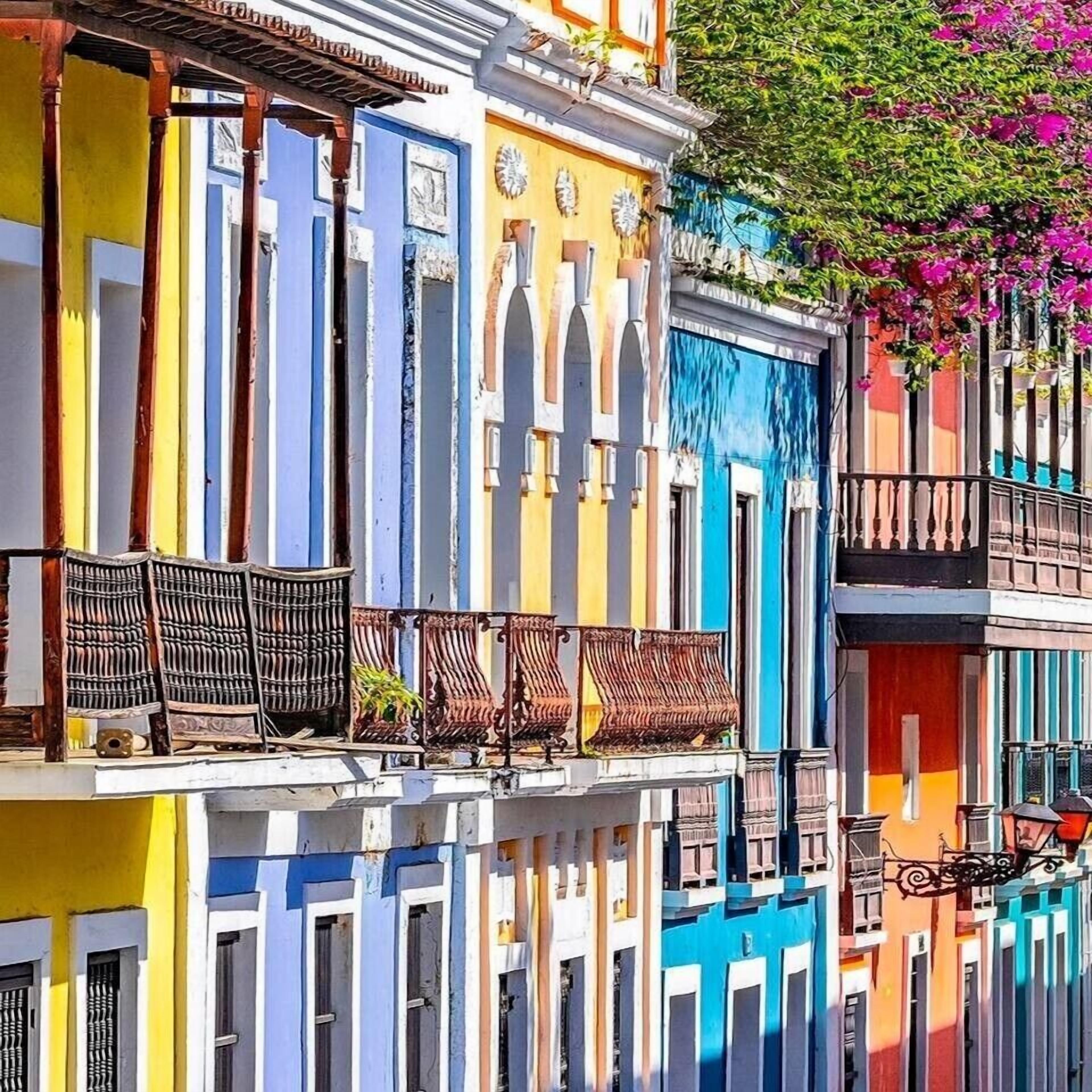A row of colorful buildings with balconies, some with plants and outdoor furniture.