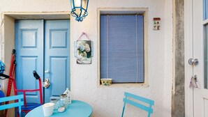 Una habitación con puerta azul, ventana con persianas, una mesa con sillas y una lámpara colgante.