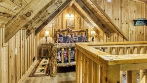 A cozy attic bedroom with wooden walls, a bed with plaid bedding, two bedside lamps, and a wooden railing. - Summer Sale! Rustic Romance Classic American Cabin Vibes! (Sevierville)