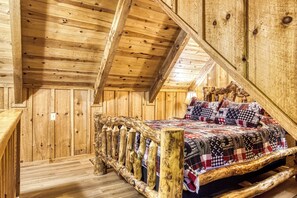 A wooden cabin interior with a bed, wooden walls, and a sloped ceiling.