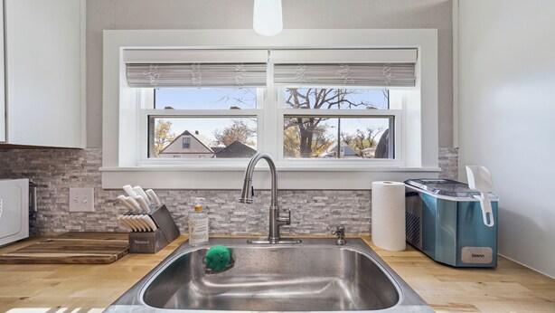 A modern kitchen with a stainless steel sink, a window with blinds, a knife block, and a toaster. - Wichita Getaway • Popcorn • Fast Wi-Fi & free Coffee bar (Wichita)