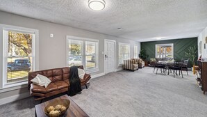 A spacious living room with a brown leather couch, a dining table with chairs, and large windows with blinds. - Wichita Getaway • Popcorn • Fast Wi-Fi & free Coffee bar (Wichita)