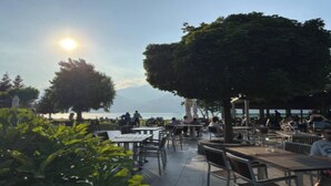 An outdoor seating area with tables and chairs, overlooking a body of water and a mountain in the distance.
