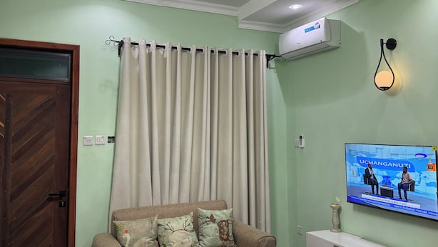 A modern living room with a sofa, a coffee table, a TV, and a ceiling with green and white geometric patterns. - Fabulous 1- self contained bedroom apartment with AC in Pwani Region (Kibaha)