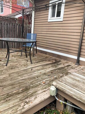 A wooden deck with a table and chairs, a window, and a utility box.