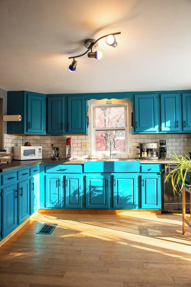 Una cocina con armarios color turquesa, microondas, cafetera y ventana con vistas a árboles.