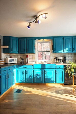 A kitchen with teal cabinets, a microwave, a coffee maker, and a window with a view of trees.
