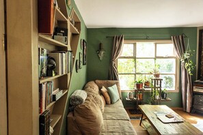 Una sala acogedora con un sofá, una estantería y un ventanal con cortinas.