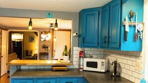 Una cocina con armarios azules, un microondas, un lavamanos y una encimera con diversos objetos.