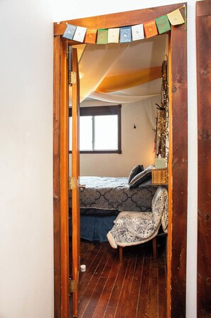 Un estrecho acceso da a un dormitorio con una cama, un sillón y una ventana.